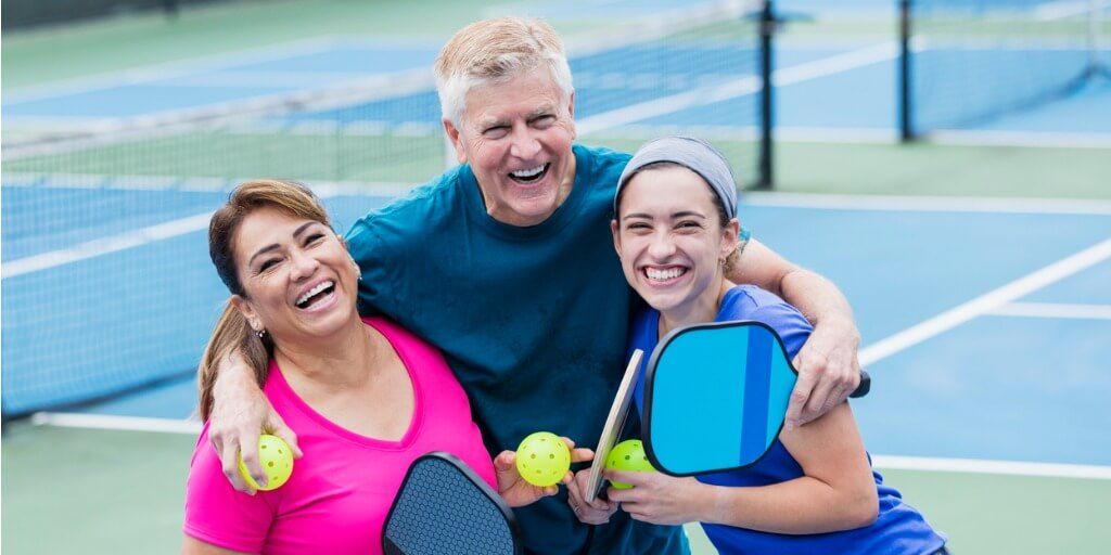 Family of three hugging and smiling on the pickleball court