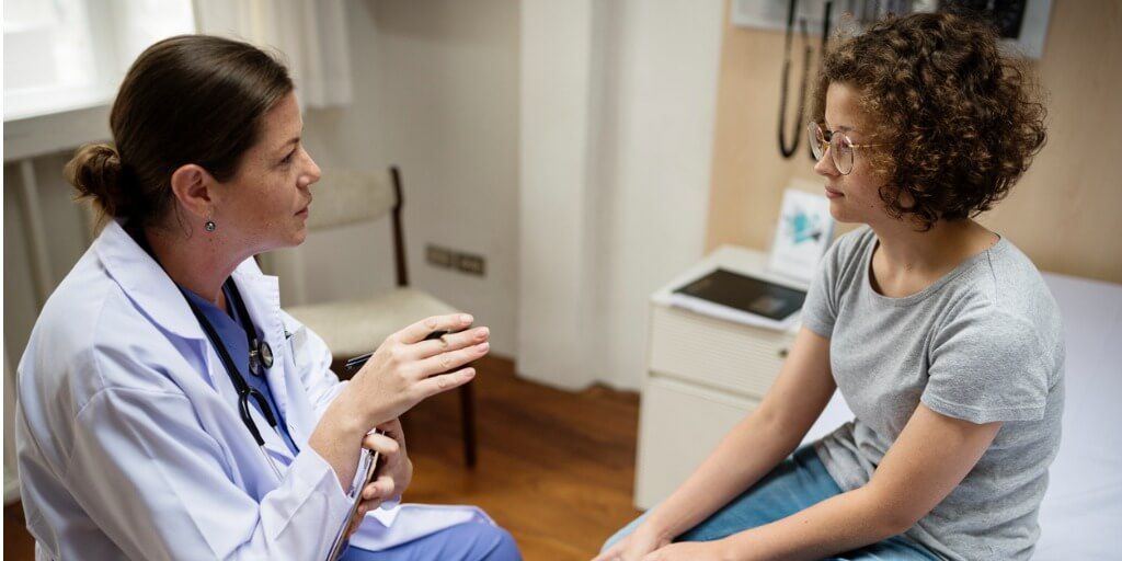 Female physician talking to female teenage patient. 