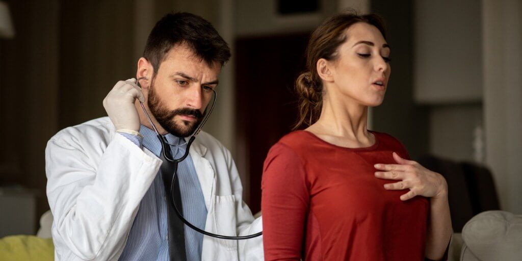 Male physician listening to lungs of female patient
