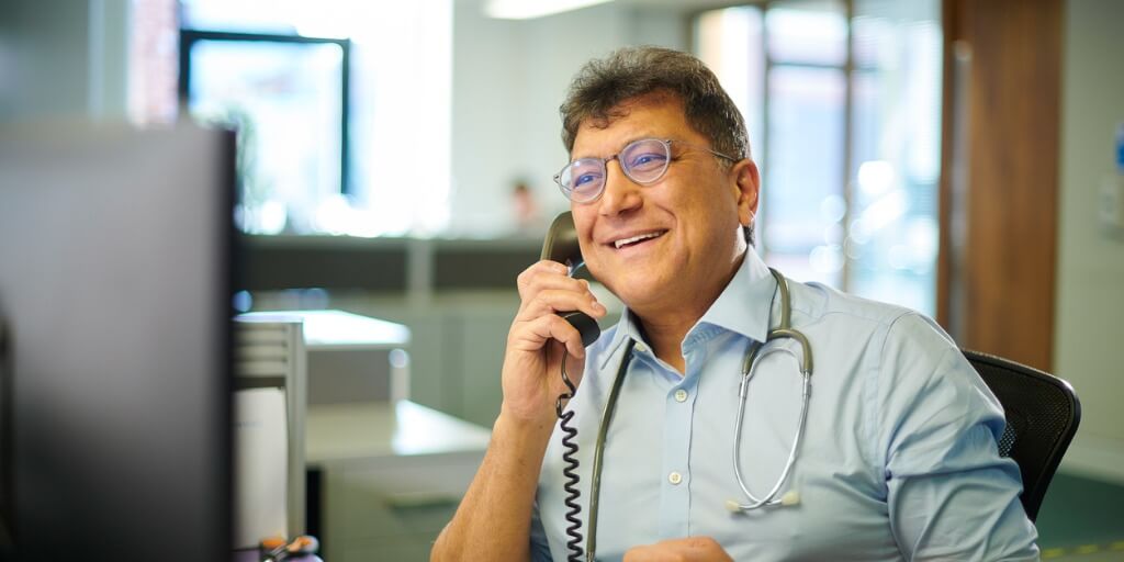 Male primary care physician on phone with patient. 