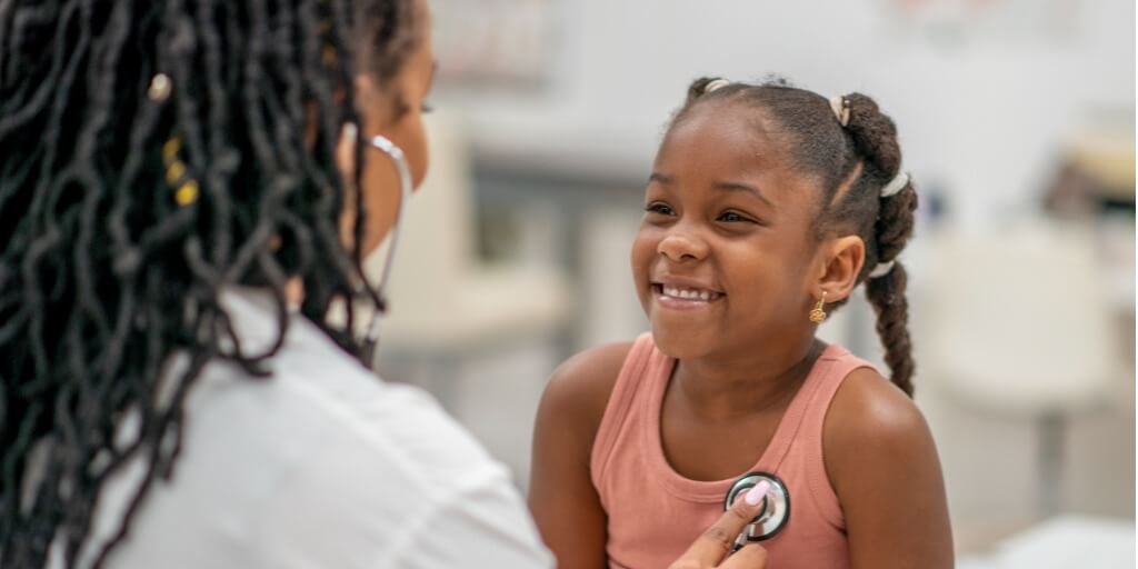 Young girl laughing while her doctor listens to her heart. 