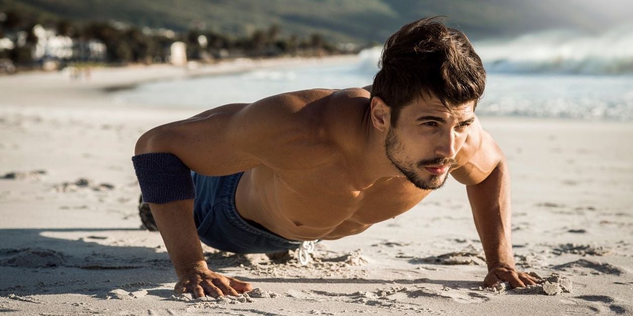 Man doing pushup exercise in sand.