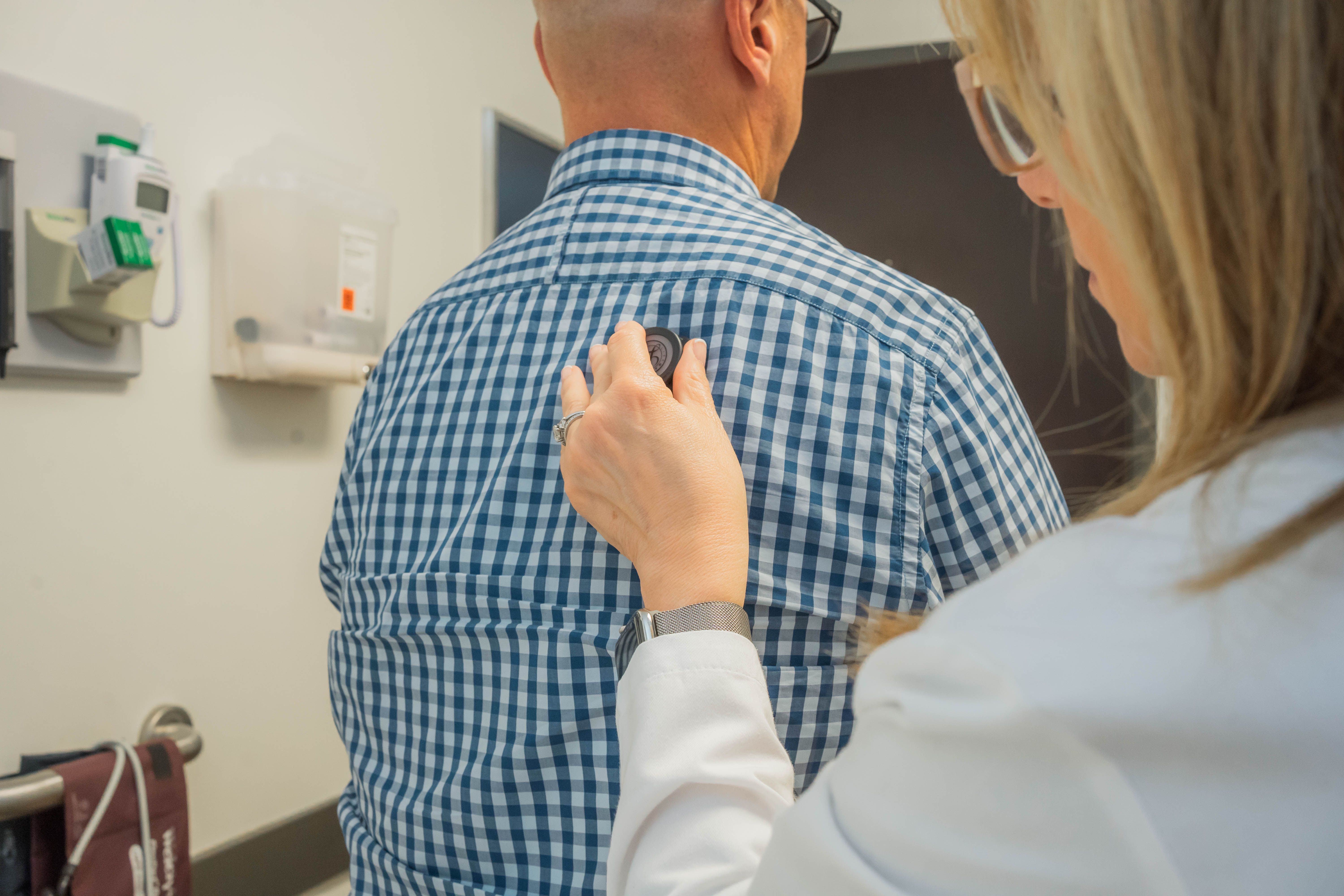 A physician places a stethoscope on a patient's back to listen