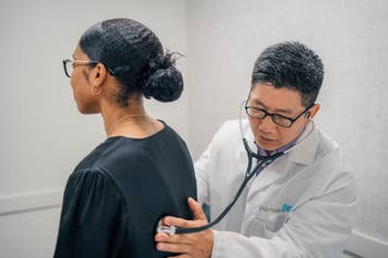 Dr. Shih listens to a patient's back with his stethoscope