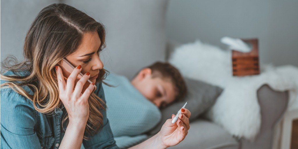 Mother checking temperature of sick son in bed