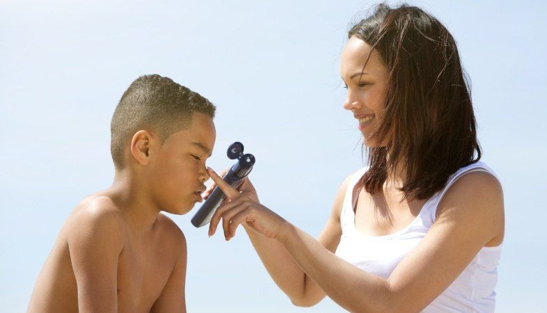 Mother applying sunscreen to child on the beach