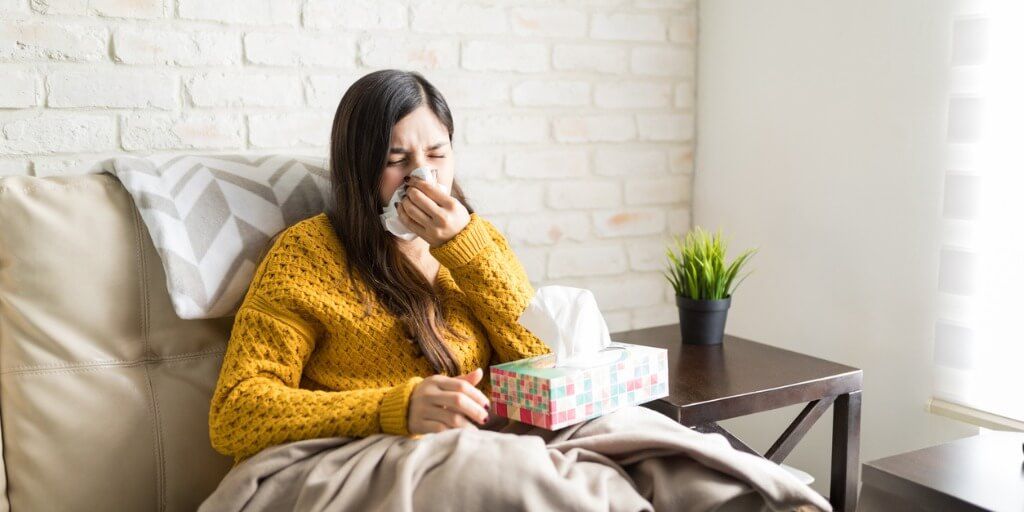 Young woman sneezing at home with a sinus infection