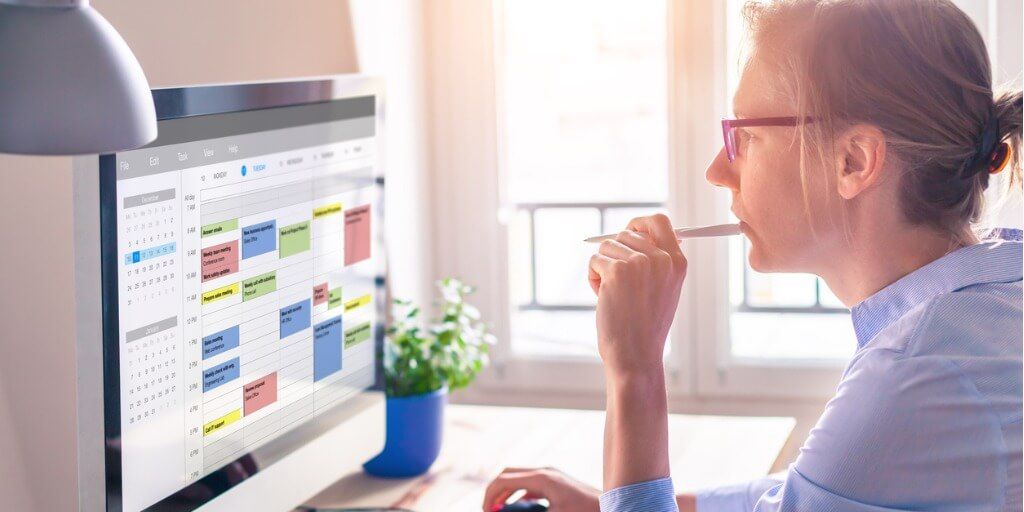 Busy professional looking at packed calendar on computer