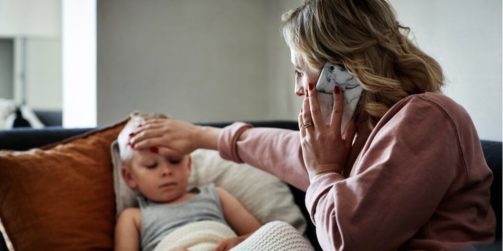 Mother feeling sick child's forehead while on phone with doctor. 